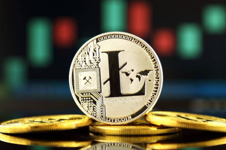 Moeda Litecoin (LTC) em prata sob moedas douradas. Fundo com luzes abstratas.